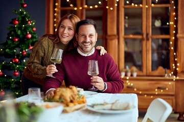 Joyful Couple Celebrates Christmas Dinner Together With Wine By Festive Tree and Warm Lights