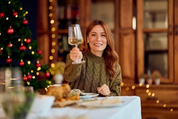 Smiling Woman Raising Glass at Festive New Year Dinner With Christmas Tree Backdrop