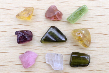 Tourmaline different color jewel stone texture on light varnished wood background. Macro closeup.