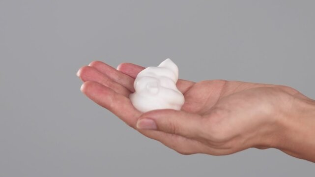 Macro close-up of hands dispensing white foam from bottle into the palm on a light background. Product application during daily skincare and beauty routine.