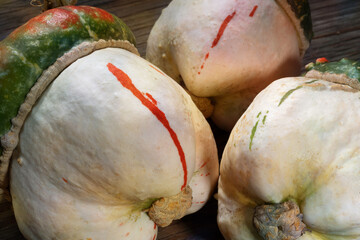 Three decorative pumpkins on a wooden table. A decorative pumpkin of the "Turkish Turban" variety. A mushroom-shaped pumpkin with a red cap.