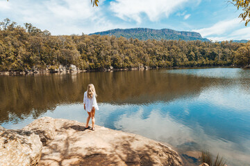 Woman in flowy white shirt stands on rock by river