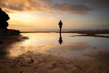 Woman and her reflection watches the sunrise