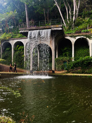 Fototapeta premium Waterfall over arches in Madeira garden park in Portugal with lush greenery and pond