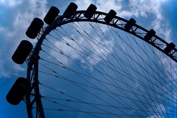 Close-up silhouette of a ferris wheel against a cloudy, moody sky. Dramatic light and textured clouds, creating a sense of atmosphere and urban minimalism. 