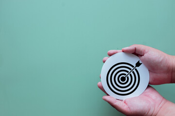 Hands holding a target icon on a green background with copy space. A concept of business goals, marketing strategy, achieving success through clear objectives, and a focused company mission.