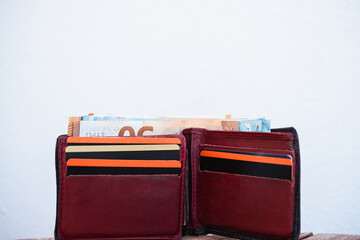 A brown leather men's wallet is open on a wooden table. In it are several credit cards and bills. Daylight