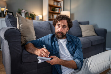 Man writing notes in notepad on living room floor