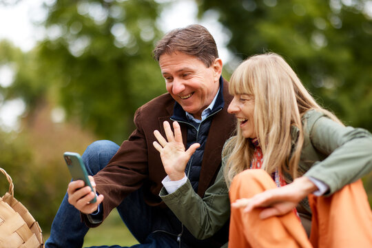 Mature couple video calling, waving hand outdoors