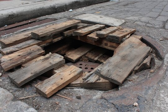 Hazardous Broken Pallet Shaft in Urban Setting: Wood Debris Exposing Manhole on Street