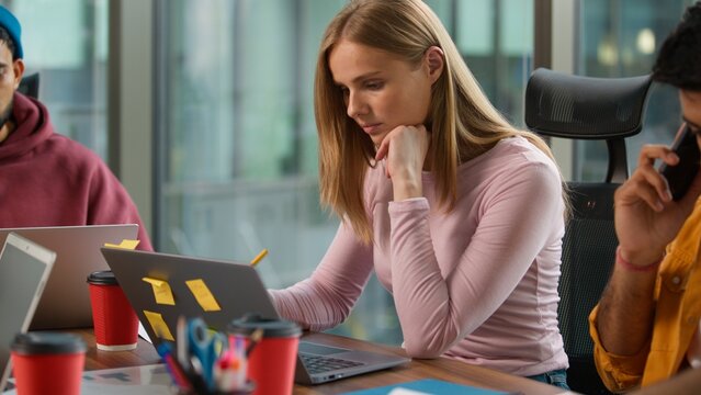 Three concentrated business professional multiracial colleagues at table informal working company busy job task Caucasian woman with laptop Indian men talking phone and reviewing diagram documents