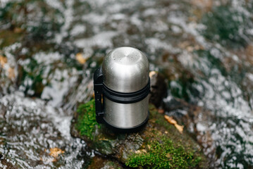 small convenient metal camping thermos for tea and other hot drinks stands alone on large stone in...