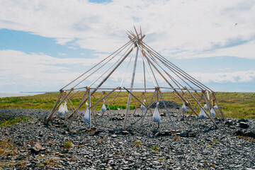 Traditional Chukchi yaranga framework in tundra near Anadyr, Chukotka, Russia, on a stony coastal plain under summer sky.
