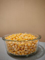 A glass bowl filled with fresh yellow corn kernels placed on a table. 