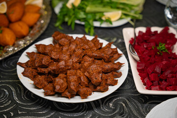 Plate of traditional cig kofte served with beet salad, greens and lemon slices. Traditional middle eastern and turkish cuisine kibbeh. Spicy bulgur raw meatballs. Table dinner concept