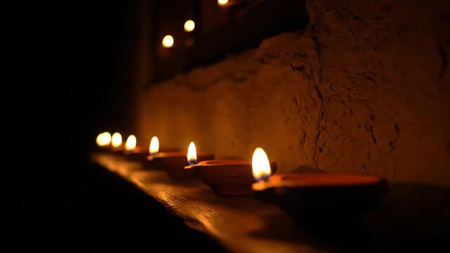 A serene row of traditional Indian oil lamps glowing in the dark.