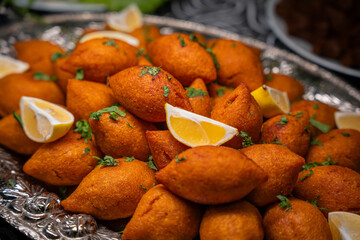 Traditional Turkish and Arap icli kofte served with lemon wedges on silver tray. Golden fried stuffed bulgur meatballs kibbeh. Popular dish in Middle Eastern cuisine. Dinner concept, close-up