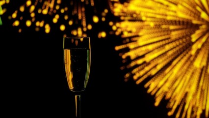 Close up of a champagne glass with golden bubbles against a backdrop of warm bokeh fireworks. A festive mood for holiday, New Year's, and Christmas parties.