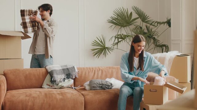 A young couple sorts through boxes in their new apartment, happily unpacking clothes and home goods as they adjust to their recent relocation to a new environment.