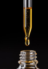 Close-up of dropper releasing yellow essential oil into glass bottle  