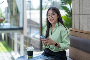 Asian freelancer woman using mobile phone in cafe and drinking matcha latte