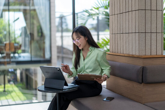 Businesswoman working remotely using tablet and clipboard in modern office lobby