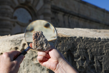 An archaeologist examines an ancient artifact with a magnifying glass amidst the ruins of an old...