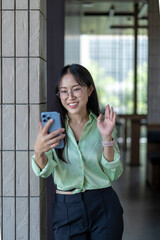 Fototapeta premium Smiling businesswoman waving while making video call on her phone in modern office