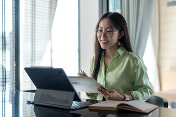 Young asian businesswoman working from home using tablet and taking notes