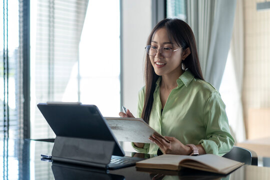 Young asian businesswoman working from home using tablet and taking notes