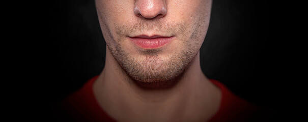 Close-up portrait of the lower half of a man s face with light stubble and natural lips against a dark background