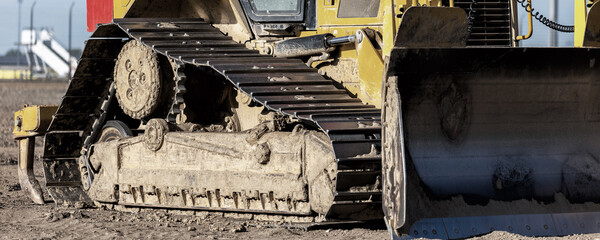 Powerful heavy yellow bulldozer standing on sandy ground construction site bright sunny day. The machine steel blade shovel heavy tracks symbolizes strength, industrial power land shaping technology