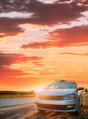 Sedan Car Parking Near Asphalt Country Road In Sunny Sunset. Sunlight Above Road In Sunrise