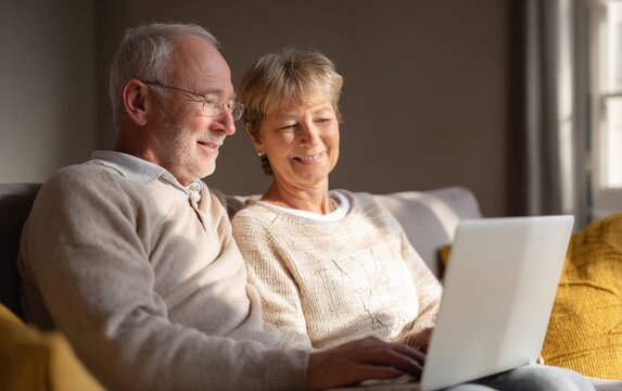 Senior couple joyfully sharing moments while using a laptop together in a cozy living room