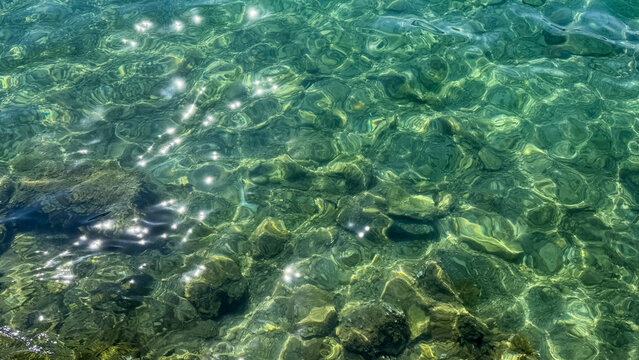 Sunlit ripples dance upon a mosaic of emerald stones, evoking Midsummer serenades and mystical water sprite folklore