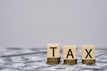 Wooden blocks spelling TAX on stacks of coins over US dollar bills represent taxation, financial planning, accounting, income reporting, and government revenue. Ideal for finance themes.