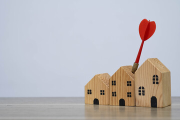 A red dart hitting the tallest wooden house represents targeted property investment, real estate strategy, and achieving homeownership goals.