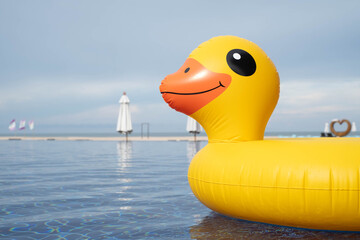 Yellow inflatable duck float in swimming pool with sea and beach background, ideal for summer holiday themes, beach resort marketing, vacation content, and playful lifestyle imagery.