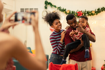Black woman using smartphone taking picture of an African family during Christmas celebration at home. Decoration background, people gathering on winter holiday and doing activities together