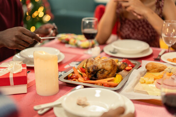 A festive Christmas dinner table with a roasted chicken or turkey, wine, and a glowing candle. Family enjoys a traditional holiday meal with a gift