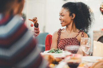 A beautiful Black woman at a Christmas dinner is smiling and enjoying a fun moment with a family at home. The family or friends are gathered at a festive table. Moment of joy and togetherness