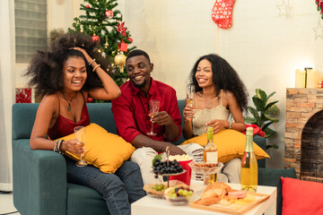 Happy Black family and friends celebrating the winter holidays at home. The group is enjoying a festive gathering, relaxing on the sofa and eating dinner. Joyful seasonal moments of togethernes