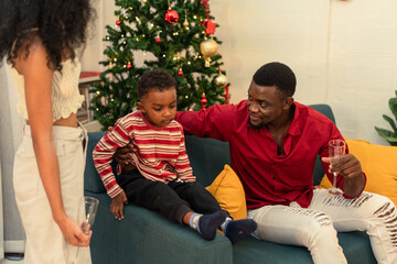 A happy Black family enjoying Christmas celebration at home. Parents and children relaxing on the sofa. The joy, togetherness, and cozy holiday spirit amidst the winter cheer and elegant decor