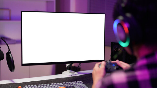 Man in dimly lit home playing video games on isolated screen gaming PC at computer desk, enjoying day off from work. Gamer battling enemies in online multiplayer shooter on mockup display
