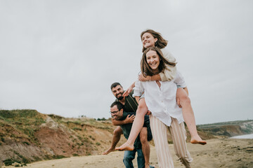 A group of people are playing on the beach, with one person carrying another on their back. Scene is lighthearted and fun, as the group of friends are enjoying each other's company
