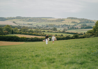 Fototapeta premium A couple is walking through a grassy field with a beautiful view of the mountains in the background