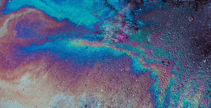 Oil spill on asphalt creating a colorful abstract pattern reflecting light with iridescent rainbow colors, showing environmental issue and pollution concept