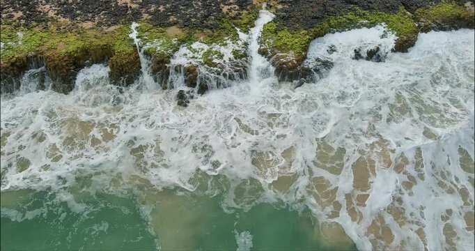 Waves crash on to the algee covered rock at Bunbury Back Beach. The wild surf creates a foam as it cascades back into the sea.