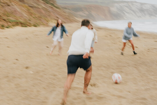 A blurry image of a group of people playing soccer on a beach. Scene is energetic and fun, as the group of people are enjoying their time together while playing the game - Powered by Adobe