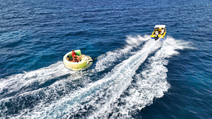 Fototapeta premium Aerial drone tracking photo of powerboat towing inflatable tubes used for water sports activities in deep blue open ocean island sea